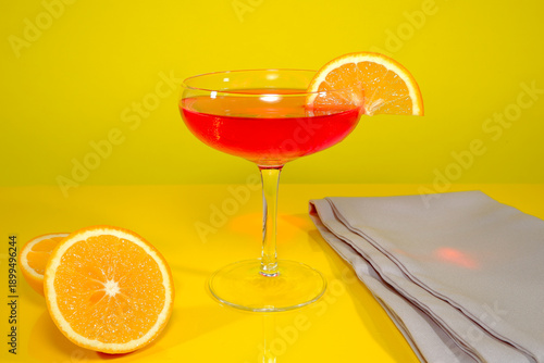Slika na platnu Vibrant red cocktail served in a classic coupe glass with a fresh orange slice g