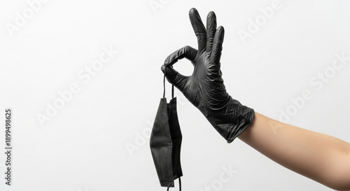 Hand in black glove holding black face mask on white background symbolizing safety and protection