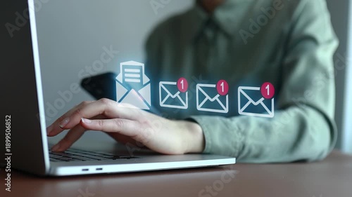 Person checks email on laptop while holding phone with notifications on screen in a simple workspace setting.