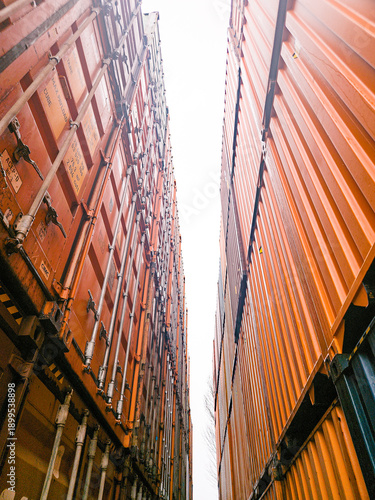 A low-angle view captures the impressive height of two stacks of vibrant orange shipping containers, creating a striking industrial vista.