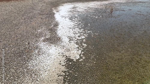 Aerial view of a lake shore covered in small white shells or pebbles creating a bright contrast with the dark mud in a winter landscape