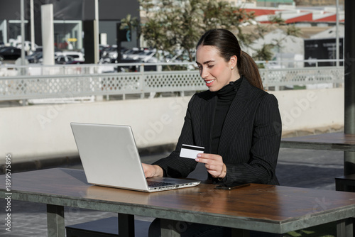 Woman using laptop while holding credit card in outdoor cafe setting