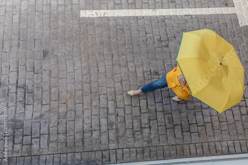 Person walking with yellow umbrella on cobblestone pavement in urban area