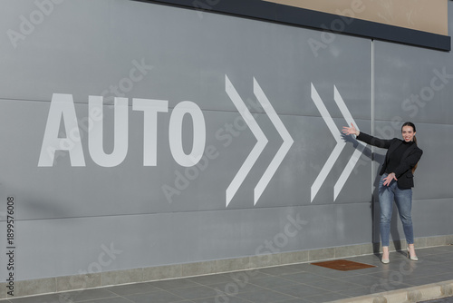 Woman gesturing towards wall with auto symbol in outdoor urban setting