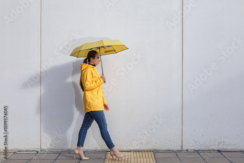 Woman walking with yellow umbrella near white wall on a sunny day
