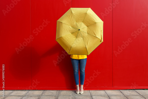 Person holding a yellow umbrella in front of a bright red wall during daytime