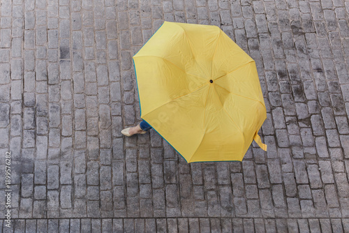 Person walking with a yellow umbrella on cobblestone street
