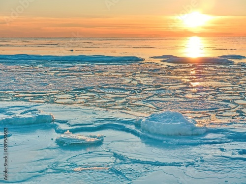 Frozen sea with cracked ice floes at golden sunrise. Winter seascape with reflections, melting ice patterns and copy space, symbol of climate change and cold nature.