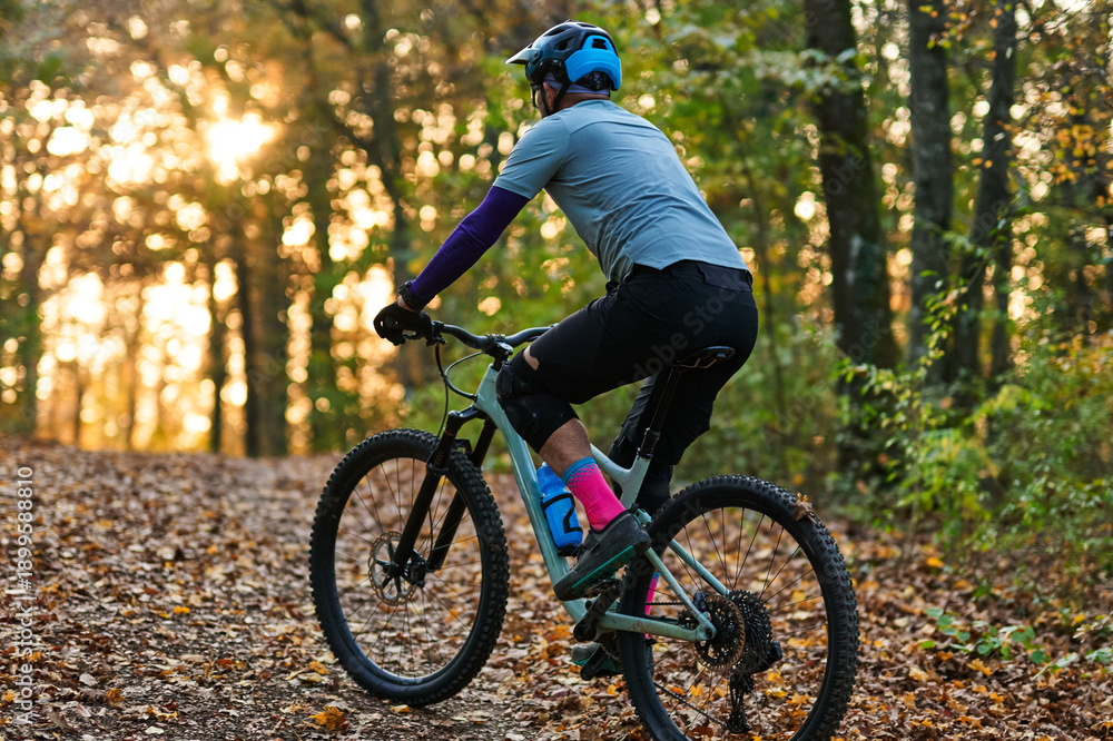 Obraz premium Mountain Biker Riding Through Autumn Forest Trail at Sunset with Sunlit Leaves