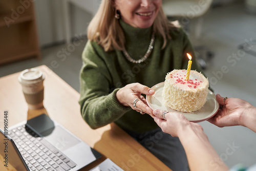 Foto Adult woman smiling while receiving birthday cake with single lit candle from an