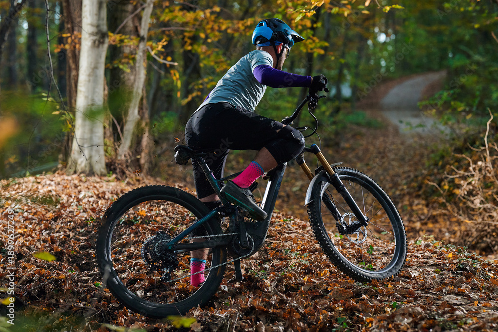 Fototapeta premium Mountain Biker Navigates Leafy Autumn Trail On Rough Forest Path At Dusk