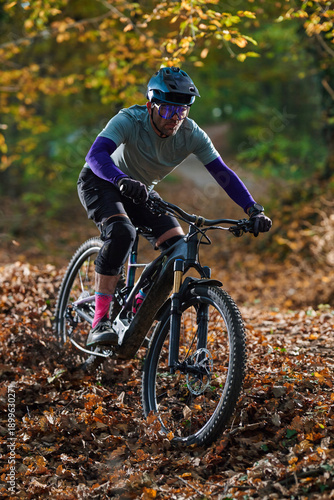 Autumn Mountain Biker In Protective Gear Rides Through Leafy Forest Trail On Rough Path