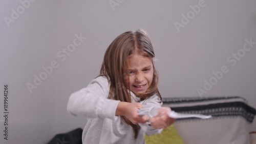 Mischievous girl tearing papers and tossing them in the air at home, enjoying a playful moment with a cheeky expression while making a fun mess