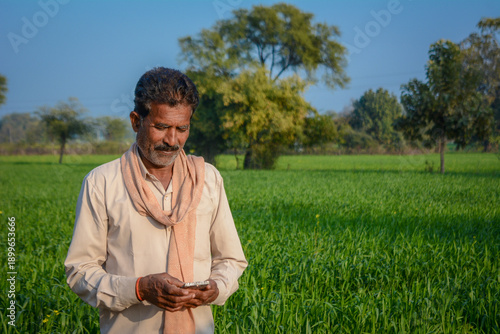 Indian farmer using mobile phone while standing in green crop field
