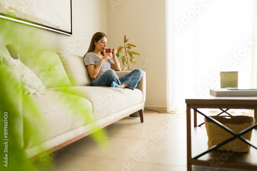 Fotografie Full length view of a woman enjoying a quiet morning, relaxing on couch in brigh