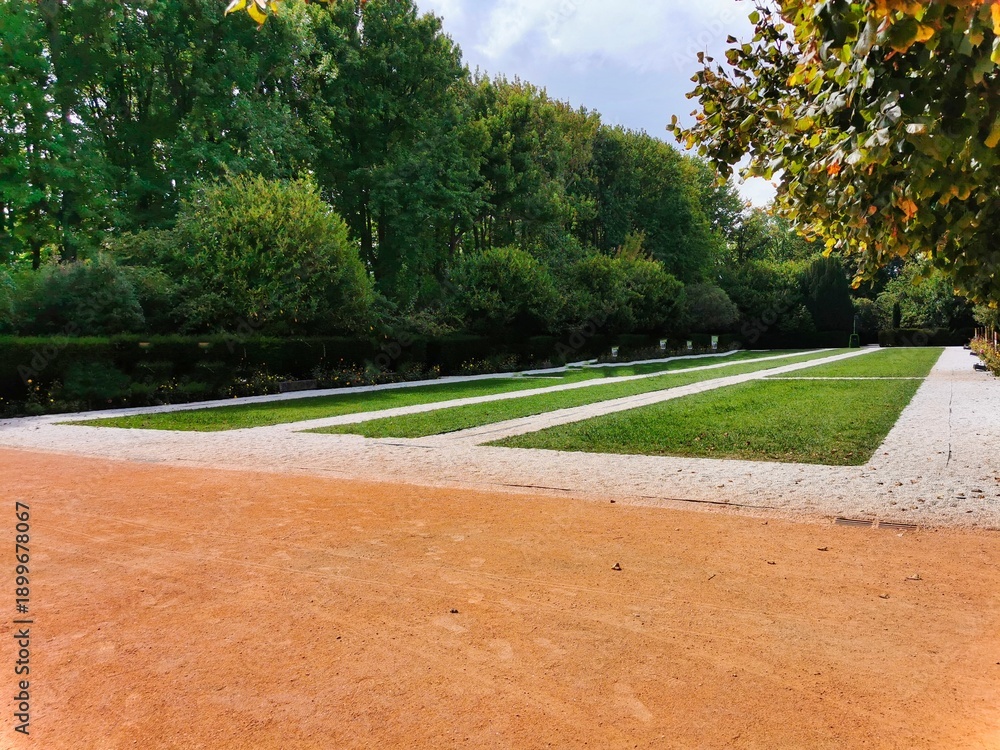Obraz premium Sidewalk in public park. Wet benches and street lamps along the avenue in the park. Petite clture et panneau dindication. Red rubber recreational jogging path in city. The morning activity.