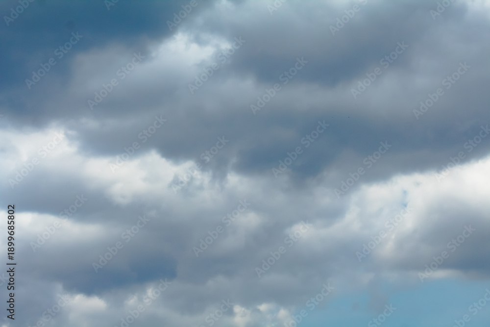 Obraz premium The sky is filled with white clouds, creating a moody atmosphere. The clouds are scattered throughout the sky, with some appearing closer to the ground and others higher up.