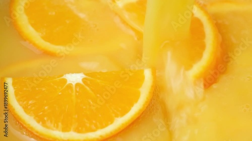 Flow of orange juice pouring fresh orange slices slow motion