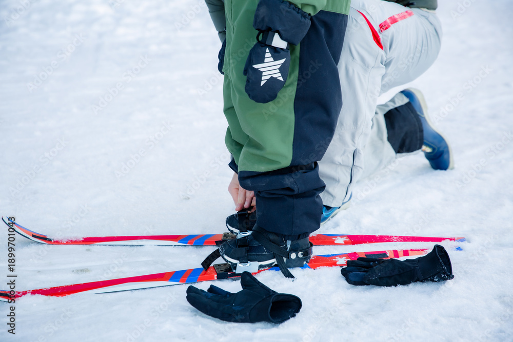Fototapeta premium Father helping son with skis in Finnish forest. Active family winter vacation, Scandinavia. Nordic lifestyle, parenting, outdoor sports. Real people.