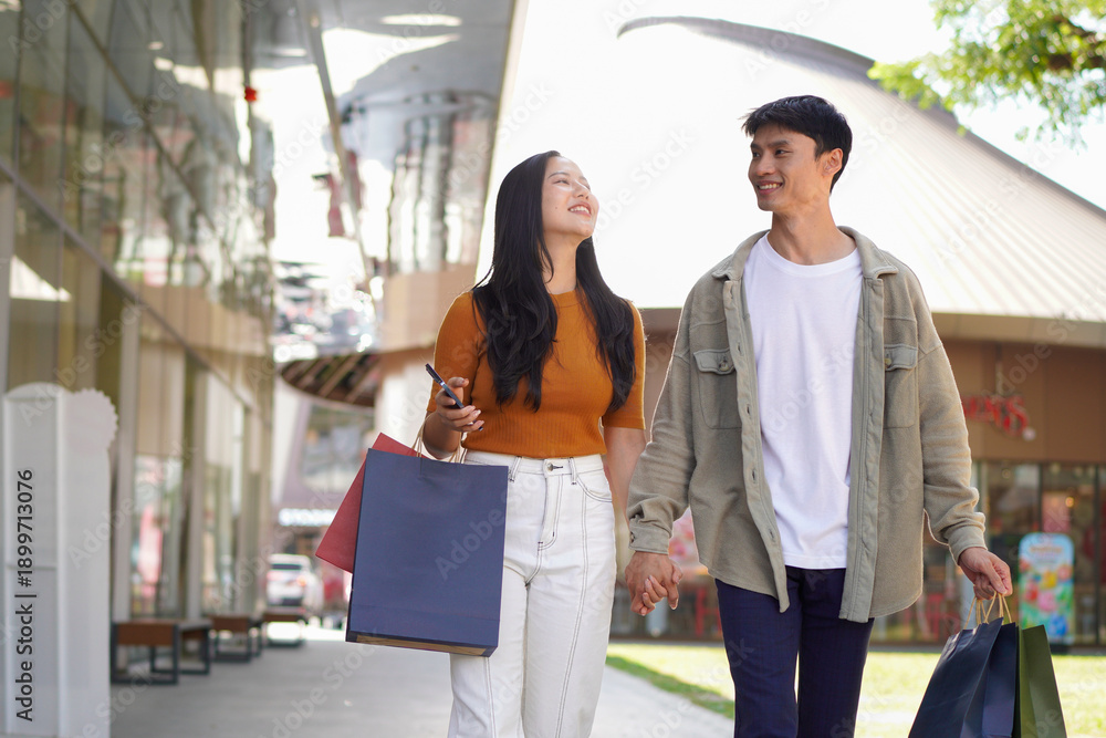 Obraz premium Beautiful couple enjoy shopping together, young couple holding shopping bags, Shopping, Couple, Love, Man and woman with shopping bags are hugging and smiling while walking down the street