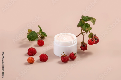 jar of hand or face cream and raspberry twigs on a beige background
