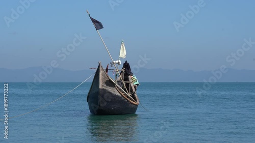 Anchored wooden fishing boat with rope on calm blue sea, Bay of Bengal, Bangladesh