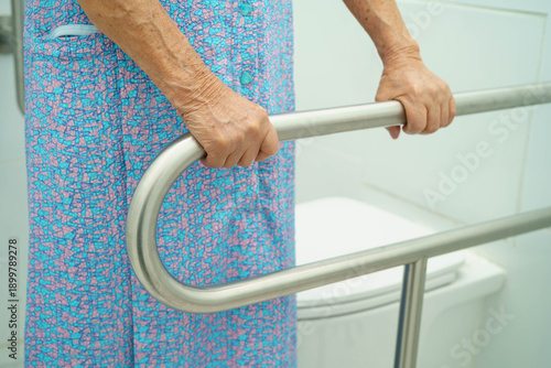 Asian elderly woman patient use toilet support rail in bathroom.