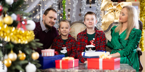 Portrait of happy family with two children celebrating Christmas next to Christmas tree