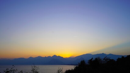 Sunset over Antalya Bay with silhouettes of the Beydağları Mountains (western Taurus Mountains). Wide landscape with sea horizon, mountain ridge and clear evening sky.