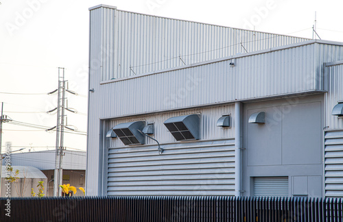 Modern industrial factory building exterior with metal corrugated wall and ventilation exhaust ducts.Minimalist silver metal warehouse facade with industrial air vents and copy space.