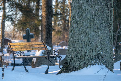 Graveyard in winter. Benches and gravestones in cemetery. Snow covered ground