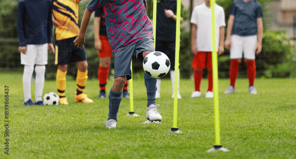 Obraz premium Youth Soccer Slalom Drill Training; Multiethnic Kids Practicing Ball Control with Poles on Grass Field