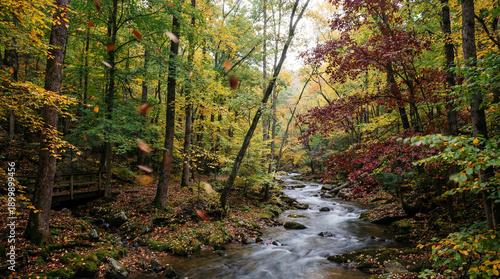 Vibrant autumnal woodland with a rushing stream and golden leaves gracefully descending near a quaint wooden bridge