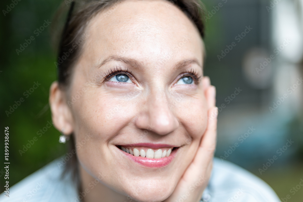 Naklejka premium Close-up detail portrait view young adult 40s beautiful smiling woman holding head chin with hand relaxed smiling sitting outdoors on day light. Female person close natural calm emotion outside