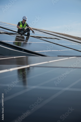 Technician installing solar panels on factory roof for green energy. A skilled technician in safety gear is working on a solar panel installation on rooftop.
