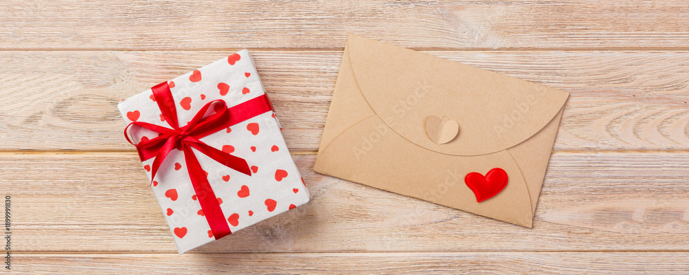 Naklejka premium Envelope Mail with Red Heart and gift box over Orange Wooden Background. Valentine Day Card, Love or Wedding Greeting Concept