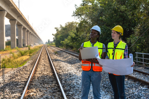 Black female locomotive and Caucasian train engineers working together in outdoor rail track inspecting rail work