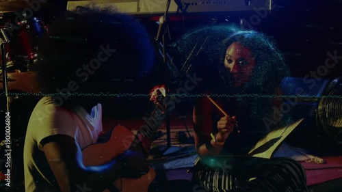 Guitarist starting to strum, female collaborator counting and tapping drum while writing song notes