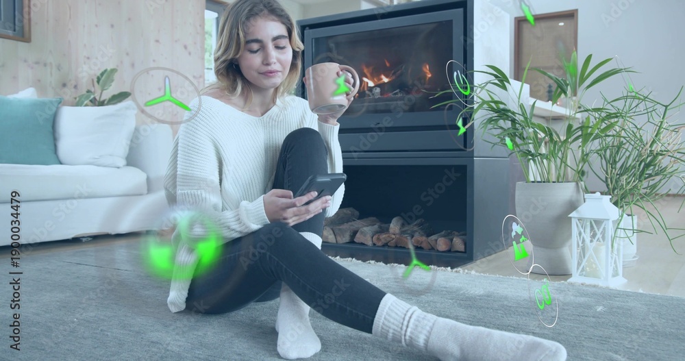Obraz premium Sitting woman holding smartphone, large mug by fireplace at home, in chunky sweater and jeans