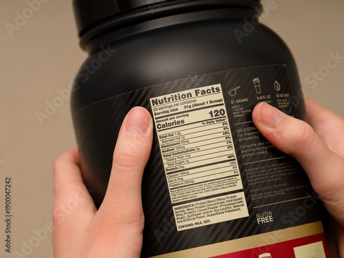 Black tub of whey protein powder with nutrition facts label in person hands. Close-up
