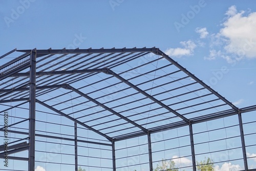 Steel frame structure of a new industrial building or warehouse under construction against a blue sky with clouds.