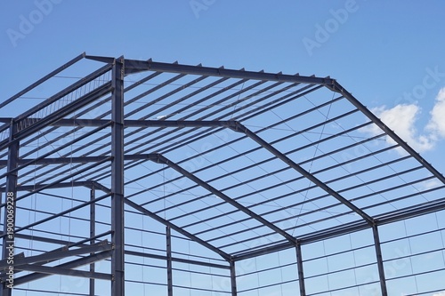Steel frame structure of a new industrial building or warehouse under construction against a blue sky with clouds.