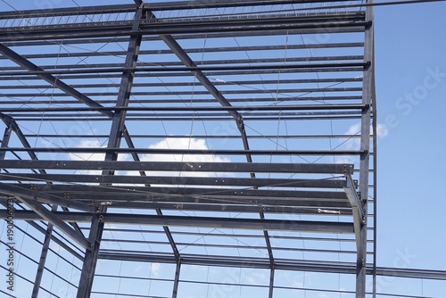 Steel frame structure of a new industrial building or warehouse under construction against a blue sky with clouds.