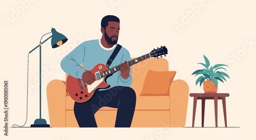 Man plays electric guitar while sitting on a couch, lamp nearby