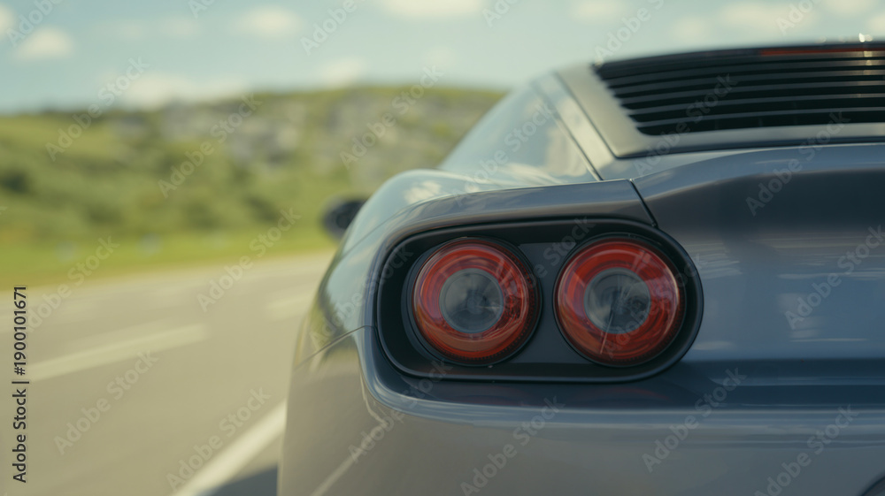 Fototapeta premium High performance silver sports car driving fast on a scenic road with motion blur background highlighting the round dual red LED taillights and aerodynamic rear design