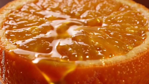 Honey being poured on a slice of orange on a brown surface