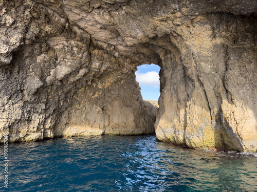 Rugged coastal cliffs and sea arches of Comino Island, Malta, near the famous Blue Lagoon. Photographed from a boat, the vibrant blue Mediterranean Sea water contrasts with the