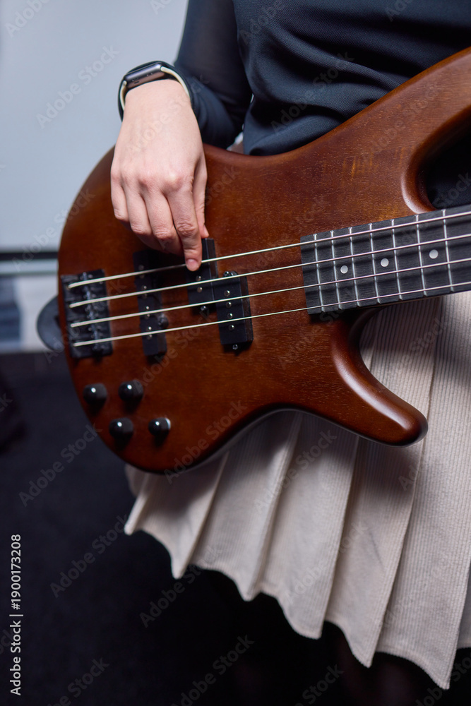 Fototapeta premium Female bassist rehearsing. Female musician with bass guitar. Female performer practicing in dim studio lighting. Female bassist preparing for performance in moody rehearsal space