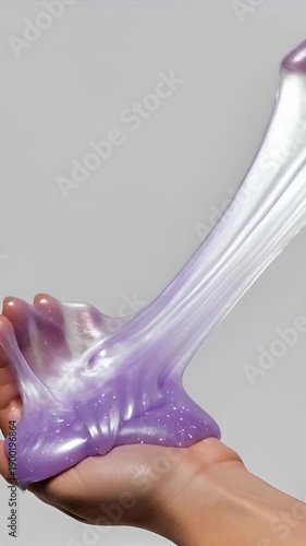 Hands playing with stretchy purple slime against gray background  