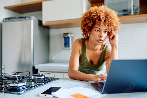 Foto Woman focused at kitchen counter, working on laptop and managing finances with b